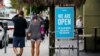 FILE - Pedestrains walk past an "open sign" at a restaurant in Long Beach, California, May 12, 2020.