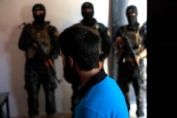 FILE - In this picture taken July 21, 2017, Kurdish soldiers from the Anti-Terrorism Units, background, stand in front a blindfolded suspected Islamic State member from Turkey at a security center, in Kobani, Syria.