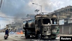 FILE - A man on a scooter rides past a damaged water tanker that was set afire during a protest by tribal groups in Churachandpur, in the northeastern Indian state of Manipur, May 4, 2023.